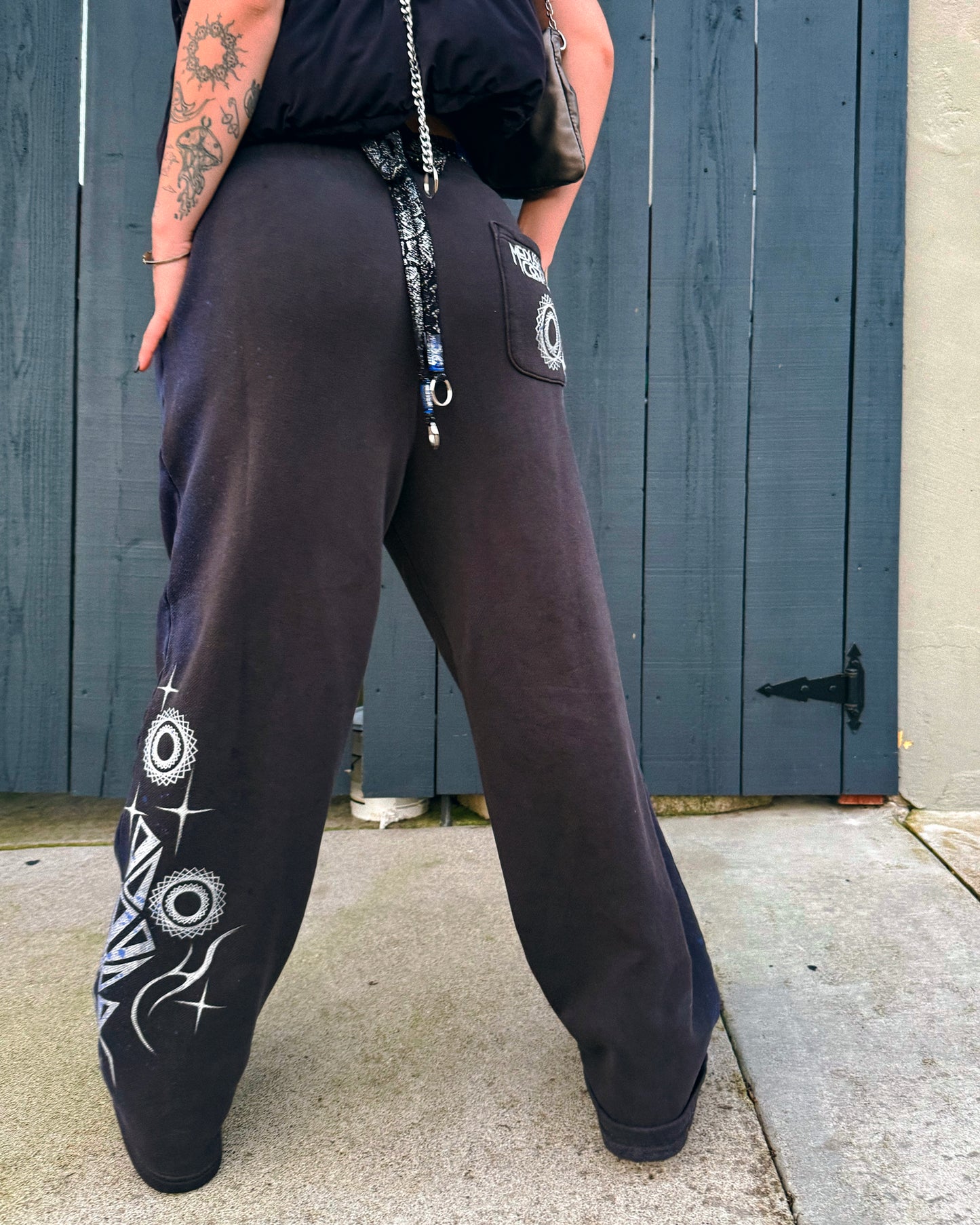 Person wearing grey sweatpants with silver hand-painted designs festivalwear streetwear