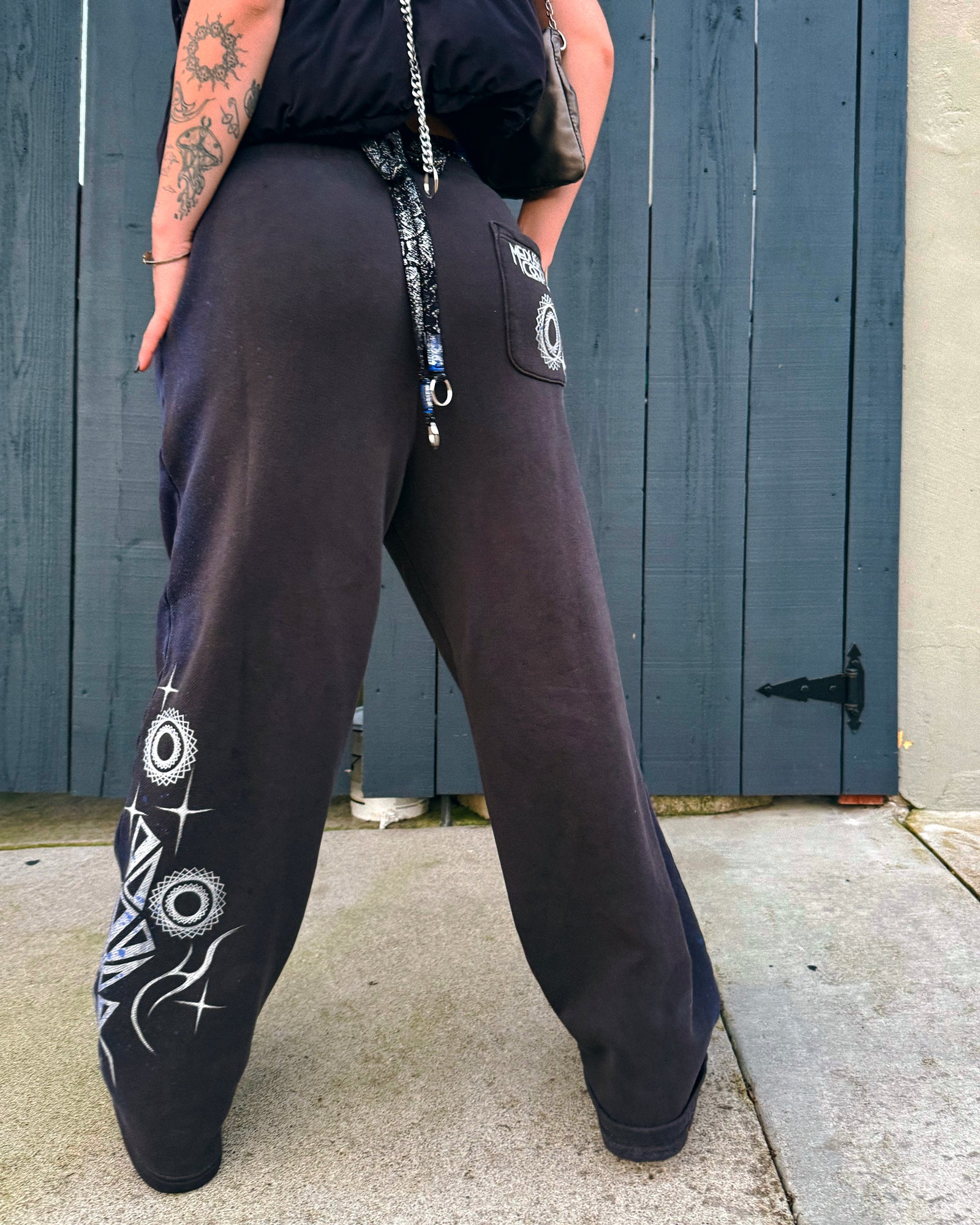Person wearing grey sweatpants with silver hand-painted designs festivalwear streetwear